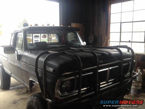 1970 Ford F-250 pickup truck with a black bull bar and roof lights, parked indoors
