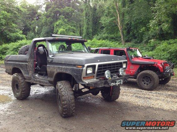 Black 1979 Ford Bronco with off-road modifications parked next to a red Jeep