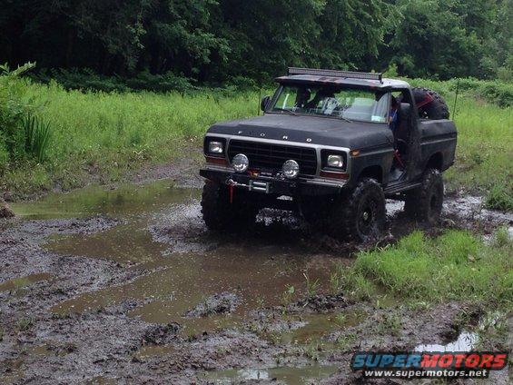 Black 1979 Ford Bronco with winch and light bar driving through mud