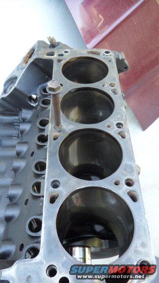 Close-up of an engine block with four cylinders visible. A bolt sticks out of the top