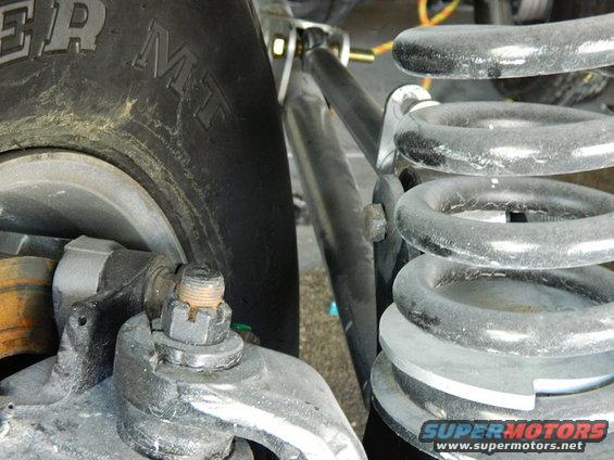 Close-up of a tire and suspension components, including a coil spring and linkage