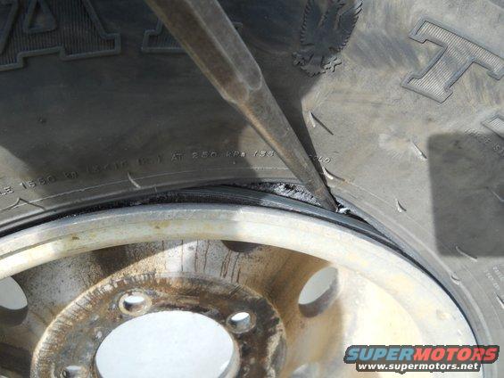 Tire bead being pried off a rusty wheel rim with a tool. Tire sidewall has text and an eagle emblem