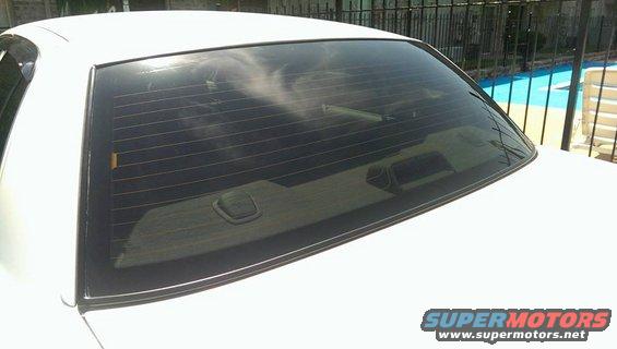 White car's rear window with defroster lines and trunk lid. Pool and fence visible in background