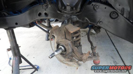 vehicle's front suspension assembly on jack stands, showing a disassembled spindle and coil spring