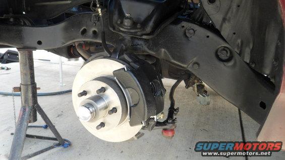 Vehicle's front suspension and brake assembly on a jack stand, showing a disc brake rotor and caliper
