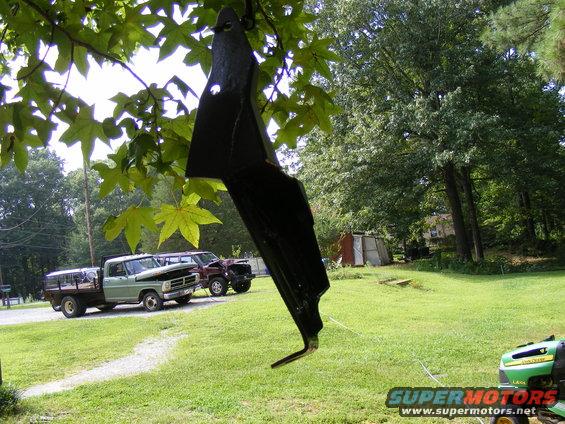 Two trucks parked in a yard, one is a flatbed and the other is a darker pickup. A lawnmower is in the foreground