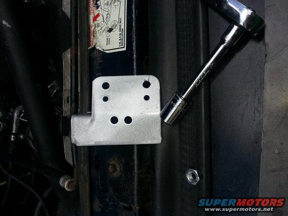 Metal bracket with four holes and a socket wrench on a dark surface