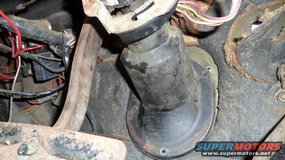 Rusty metal and black rubber boot around a steering column with visible wiring and a fuse box