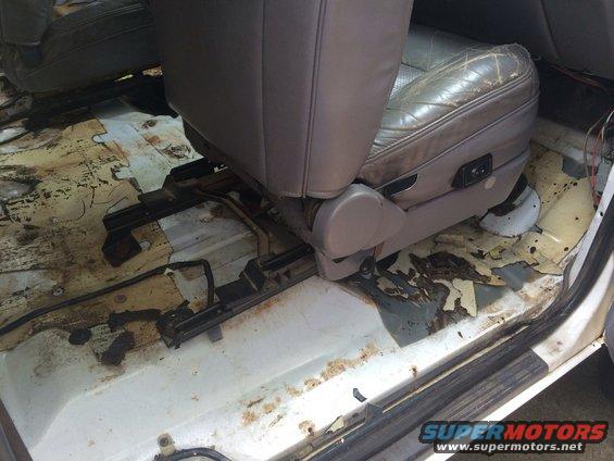 Car interior with torn leather seat and rusted floor panels