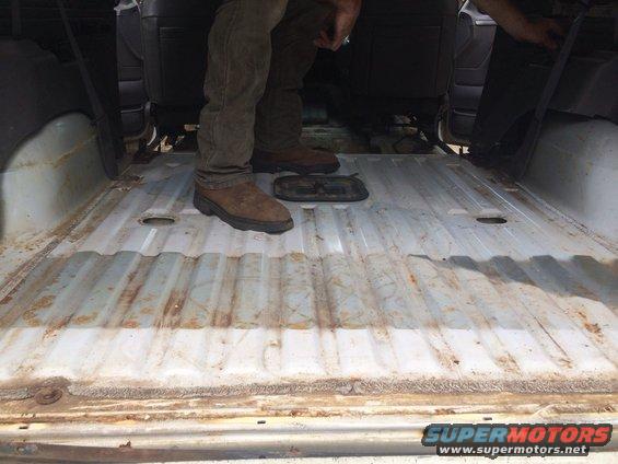 Interior cargo area with ribbed metal floor, showing two people standing. A small black object is on the floor