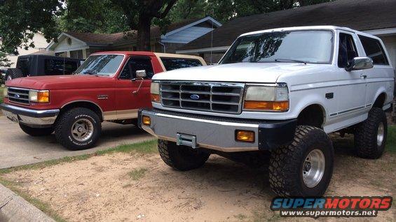 White 1994 Ford Bronco with lifted suspension parked next to a red Bronco
