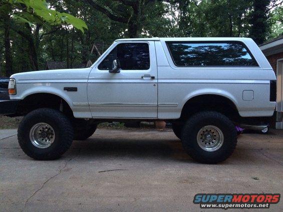 White Ford Bronco with lifted suspension and large tires parked on a concrete driveway