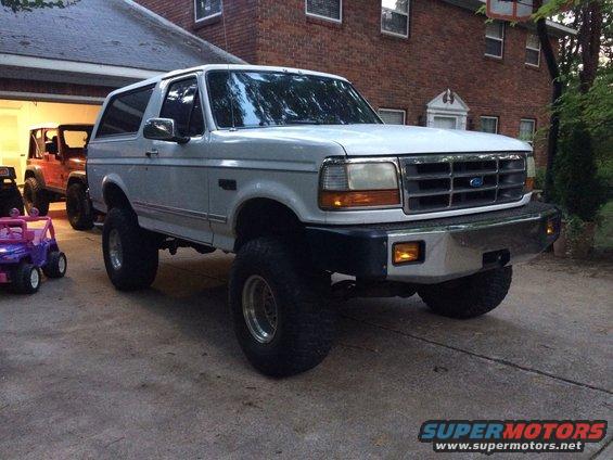 Lifted white 1994 Ford Bronco parked in driveway, red Jeep visible in garage