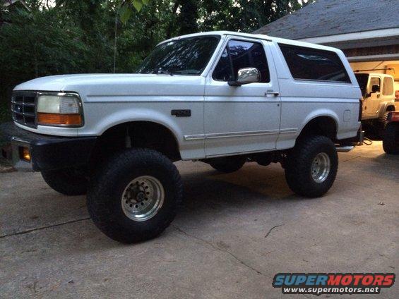 White lifted Ford Bronco parked outside a garage, another vehicle visible behind it