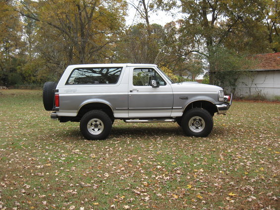 Side view of a two-tone silver and white Ford Bronco parked on a grassy lawn with fallen leaves
