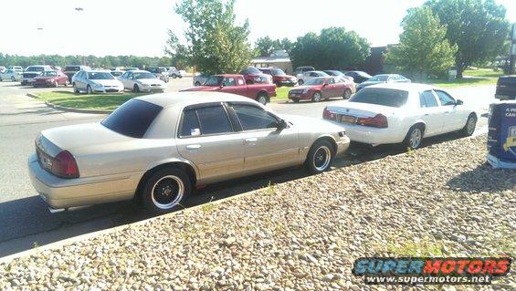 Gold sedan and white sedan parked on a street with a gravel shoulder