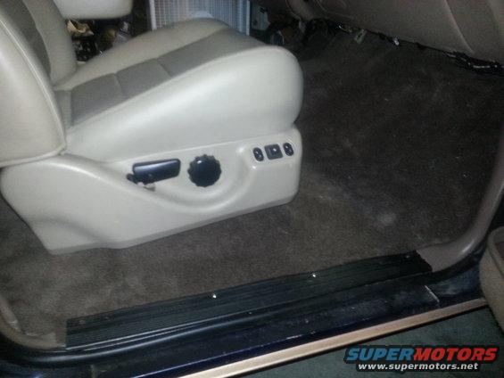 Vehicle interior showing a power seat base with adjustment controls and dark carpet