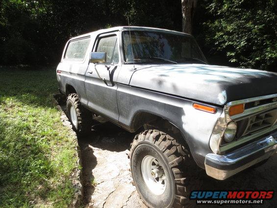 Ford Bronco with large tires, primer gray paint, parked on dirt and grass