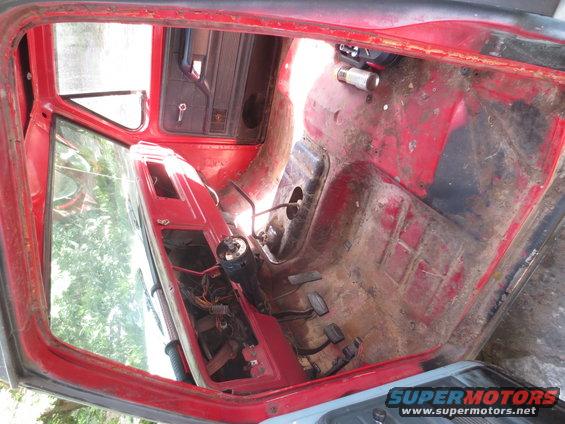 Interior view of a red vehicle, showing the floor, pedals, and part of the dashboard. The interior is stripped down