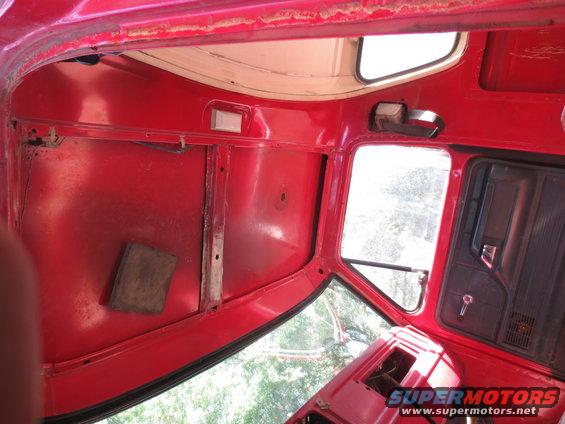 Red interior of a vehicle, showing the roof, door panel, and windows. Some rust is visible on the roof edge