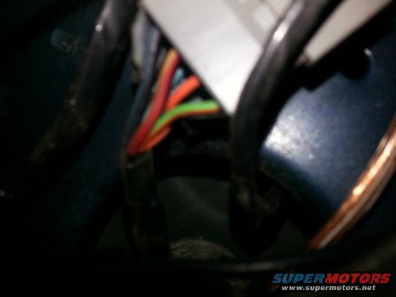 Close-up of a wiring harness with red, orange, and green wires connected to a white connector