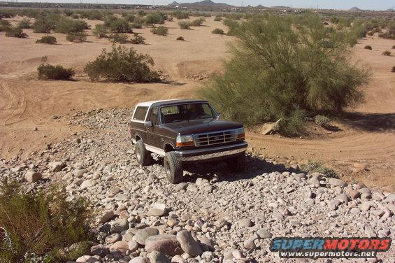 Dark brown 1992 Ford Bronco with a white top parked on a rocky desert trail