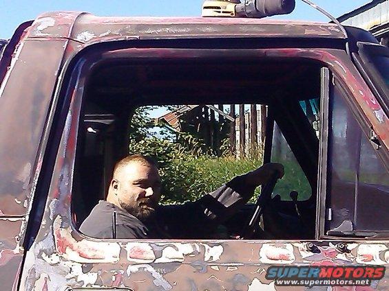 Man sits in the interior of a weathered, rusty truck cab