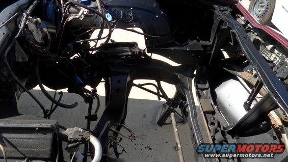 Vehicle frame and engine bay components, partially disassembled. A wheel is visible on the right