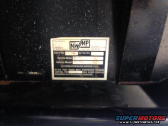 Close-up of a NWMP emissions label on a vehicle part. Shows vehicle make and model fields