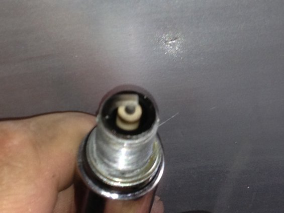 Spark plug held in a hand against a gray background