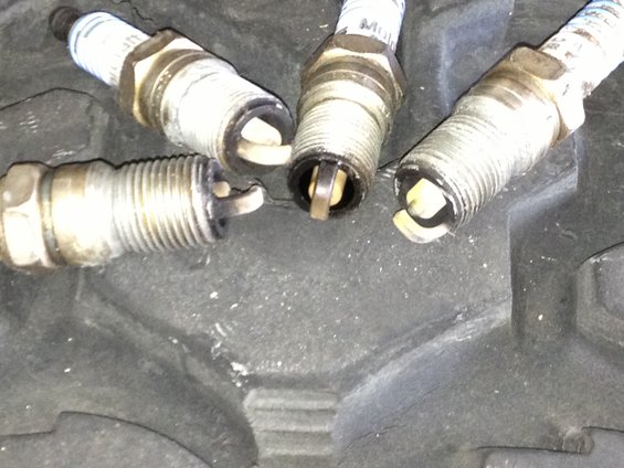 Four used spark plugs resting on a dark, textured surface