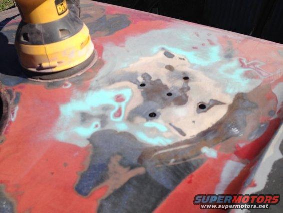 Orbital sander working on a red car body panel with primer and rust showing through