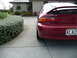 1993 Mazda MX-3 - Rear view of a red 1993 Mazda MX-3 with a spoiler, parked on a driveway.