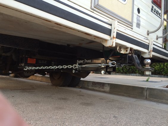 Trailer hitch extension with chains and ball mount attached to the underside of a camper