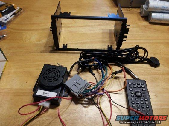 Car stereo mounting bracket, wiring harness, remote, and speaker module on a wooden surface