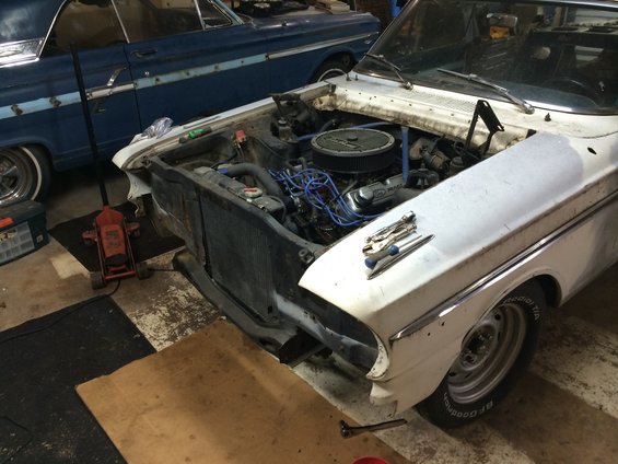 White 1964 Ford Fairlane with front end disassembled, engine visible, parked next to a blue car