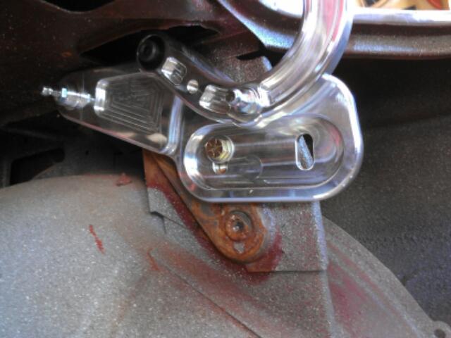 Close-up of a polished chrome linkage attached to a grey, textured component with red markings