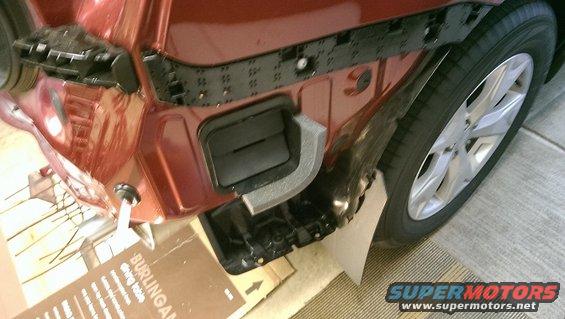 Car's rear bumper removed, showing internal mounting points and foam insulation. Tire and wheel visible
