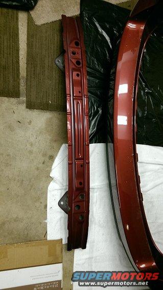 Red metallic car body panel and a dark red metal reinforcement beam with mounting brackets