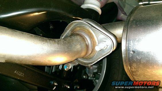 Exhaust pipe flange connection with bolts and gasket. Part number 4422D visible on suspension arm