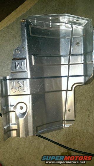 Metal underbody shield with 'M' and 'RT' markings. Part of a vehicle's undercarriage