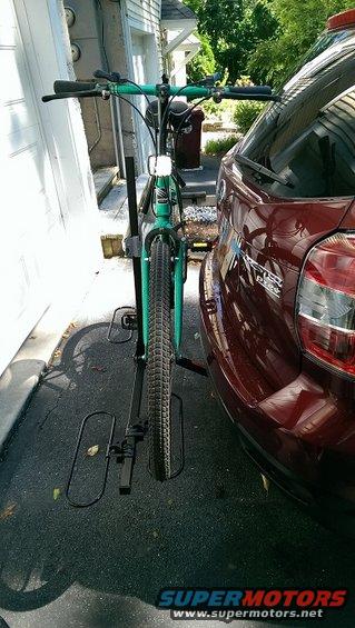 Green bicycle mounted on a black hitch rack, attached to the rear of a dark red SUV