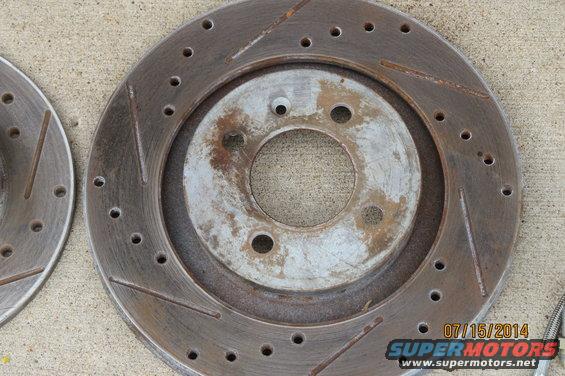 Slotted and drilled brake rotor with rust and wear marks. Date stamp '07/15/2014' and 'SUPERMOTORS.NET' visible