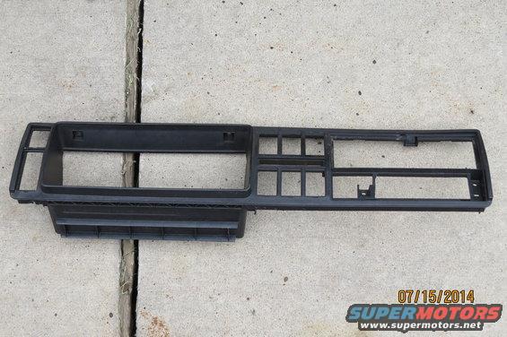 Black plastic dashboard trim piece with openings for gauges and vents