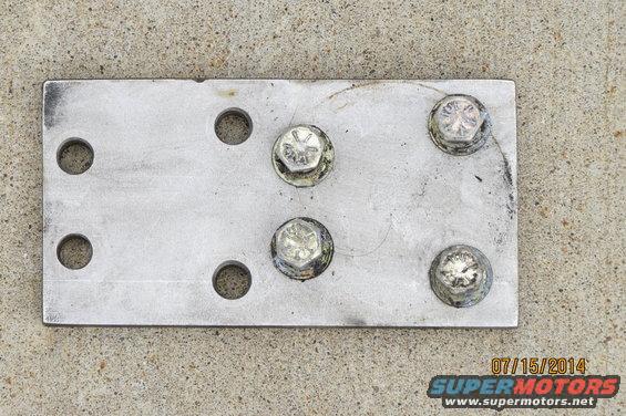 Metal plate with six bolt holes and five bolts attached, resting on concrete