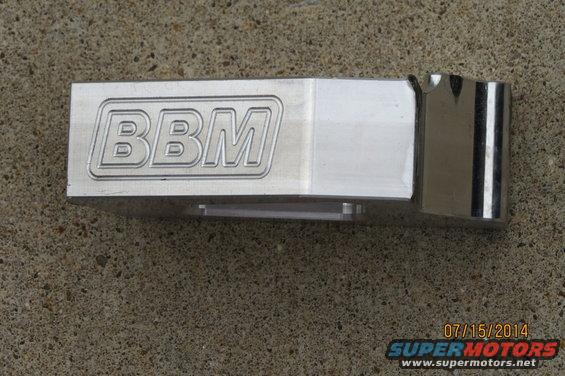 Metal part with engraved 'BBM' logo, resting on concrete