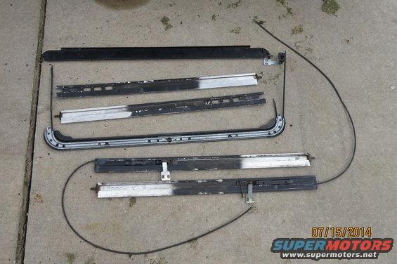 Disassembled sunroof components including tracks and cables laid out on concrete