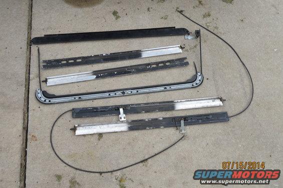 Disassembled sunroof tracks and cables laid out on concrete