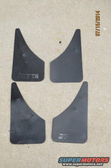 Four black mud flaps with "JETTA" embossed on two of them, laid out on a concrete surface