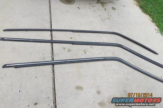 three metal trim pieces for car windows laid out on concrete
